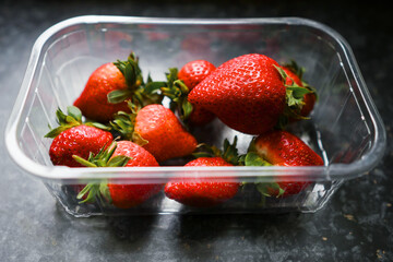Plastic tray with fresh washed strawberry on a dark table surface. Produce product. Food industry. Selective focus