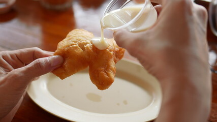 Hand hold deep fried dough or Patongkoh dipping  sweetened condensed milk.