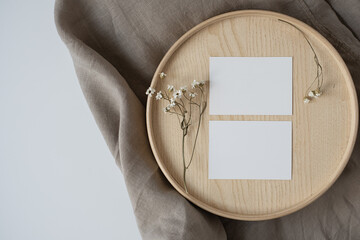 Blank paper sheet cards with mockup copy space and dry flowers on wooden casket and grey linen...