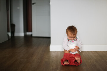 Funny kid Toddler sits on a pot with toilet paper, concept of teaching pot, child autonomy. Baby on a pink pot with a roll of toilet paper in a real Scandinavian interior.