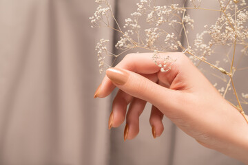 Female hand with glitter beige nail design. Female hand hold dry autumn flower. Woman hand on beige fabric background