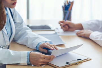 Two asian women doctors discuss meeting doctor's office medical clinic looking x-ray film consulting patient disease. Asian medical lab young women talking together discussing healthcare teamwork