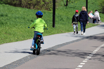Obraz premium Little boy rides a bicycle on a street in summer park on walking people background