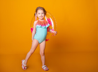 Funny little girl in swimming suit with swimming inflatable ring smiling having fun on yellow background.