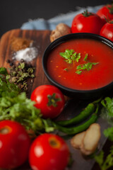 Close-up of Indian Homemade fresh and healthy tomato soup garnished with fresh coriander leaves and ingredients and herbs, served in a black bowl over the wooden top background. 