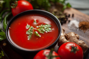 Close-up of Indian Homemade fresh and healthy tomato soup garnished with fresh coriander leaves and ingredients and herbs, served in a black bowl over the wooden top background. 
