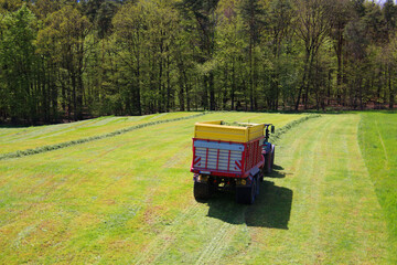 Tractor with trailer collecting hay from a meadow in spring (Swabian Alp, Germany)