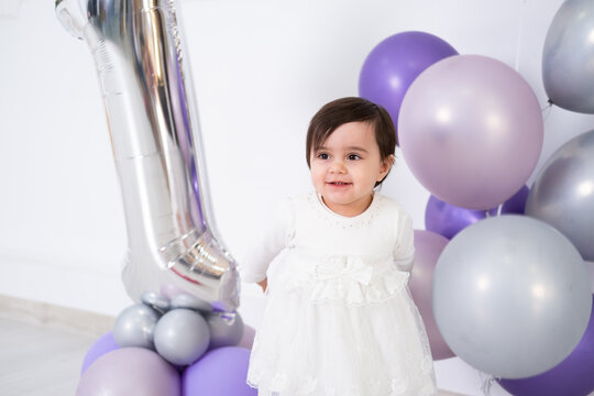 baby girl in white dress celebrating her first birthday with cake and balloons