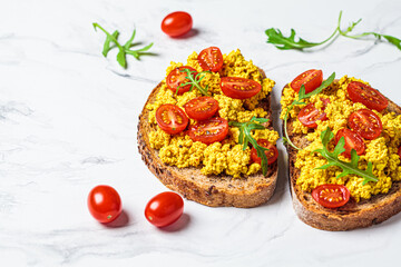 Tofu scrambled toast with tomatoes and arugula, white marble background. Plant based diet concept.