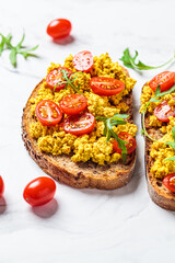 Tofu scrambled toast with tomatoes and arugula, white marble background. Plant based diet concept.