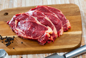Raw piece of beef tenderloin with spices on wooden cutting board on light background