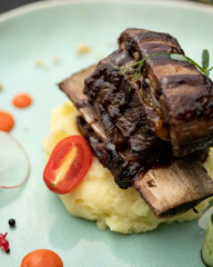 Fried pork ribs on pillow of mashed potatoes with tomato. Close up shot of mouth-watering dish.