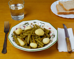 Tasty Green beans and potatoes on a plate decorated with cutlery, a glass of water and two Toasted bread slices