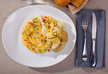 Top view of vegetable omelet with garnish of baked cauliflower sprinkled with grated cheese on white plate..