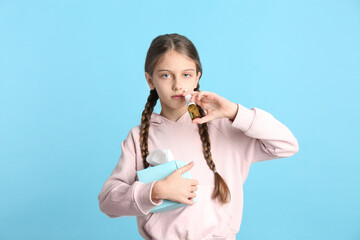 Sick little girl using nasal spray on light blue background