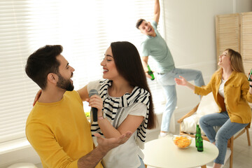 Happy couple singing karaoke with friends at home