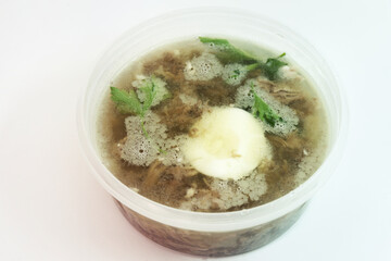 aspic with meat, eggs and fresh parsley, made with thick and rich nutritious bone broth, frozen in round transparent plastic food container