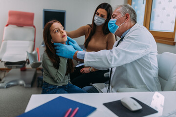 Pediatrician doctor examining a young female patient during pandemic