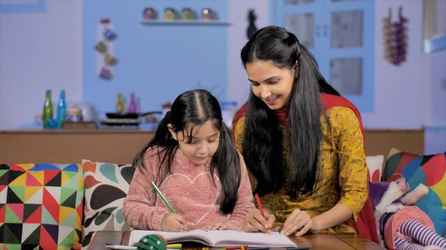 Young Indian mother teaching her school-going daughter - togetherness and bonding. Medium shot of a young art teacher helping a little child with her drawings - hobby and relaxation
