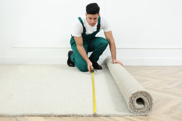 Worker with measuring tape installing new carpet indoors
