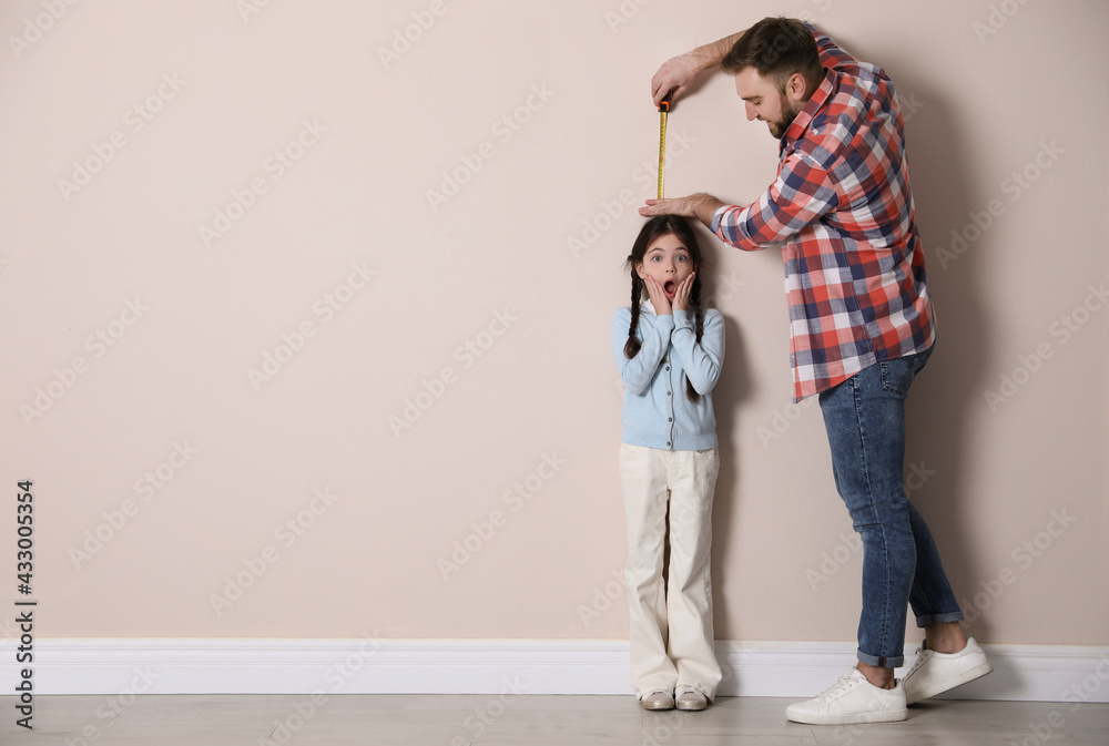 Poster Father measuring daughter's height near beige wall indoors, space for text