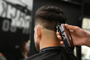 Professional barber making stylish haircut in salon, closeup