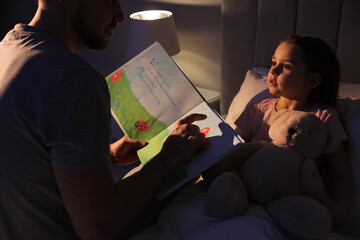 Father reading bedtime story to his daughter at home - obrazy, fototapety, plakaty