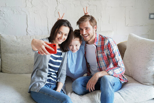 Beautiful young family with little child taking a selfie with a smartphone at home on the couch.