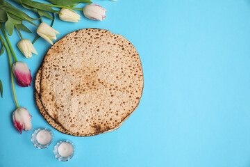 Tasty matzos, tulips and candles on light blue background, flat lay with space for text. Passover (Pesach) celebration