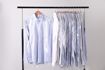 Hangers with shirts in dry cleaning plastic bags on rack against light background