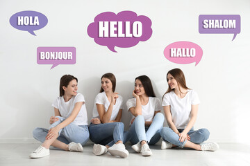 Happy women sitting near light wall and illustration of speech bubbles with word Hello written in different languages © New Africa