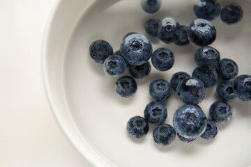 Closeup top view above Soaking heap group fresh organic picked blueberries with cold water mixed vinegar in a white bowl background. Washing for reduce and remove bacterial before eating concept