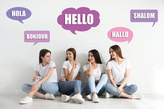 Happy women sitting near light wall and illustration of speech bubbles with word Hello written in different languages