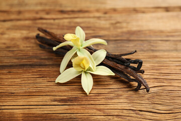 Aromatic vanilla sticks and flowers on wooden table, closeup
