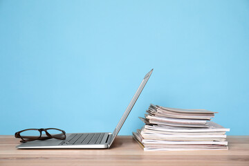 Laptop, glasses and stack of magazines on wooden table
