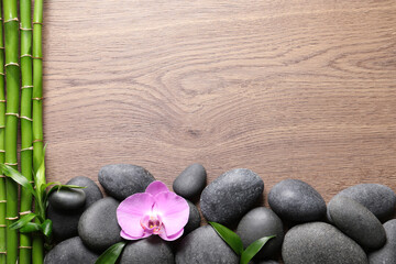 Fototapeta na wymiar Spa stones, beautiful orchid flower and bamboo stems on wooden table, flat lay. Space for text