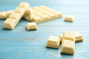 Pieces of tasty sweet chocolate on light blue wooden table, closeup. Space for text