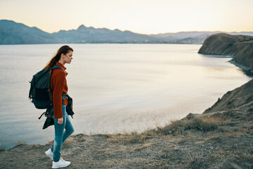 traveler in a sweater with a backpack in jeans and sneakers on the beach near the sea in the mountains