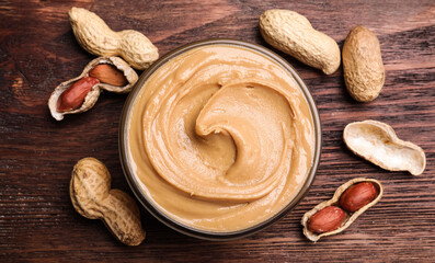 Fototapeta premium Yummy peanut butter in glass bowl on wooden table, flat lay