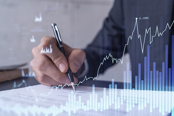 A client in formal wear is signing the contract to invest money in stock market. Internet trading and wealth management concept. Forex and financial hologram chart over the desk.