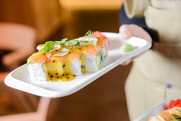 Sushi Set: sashimi and sushi rolls served in a white plate by waiter in restaurant. Eating out...