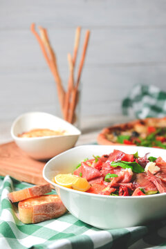 Prosciutto and arugula salad in a white bowl and lasagna over wooden background.