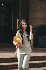 A beautiful, tanned, sexy southern beauty stands on a motley background surrounded by palm leaves and holds a wooden bowl with lemons in her hands.