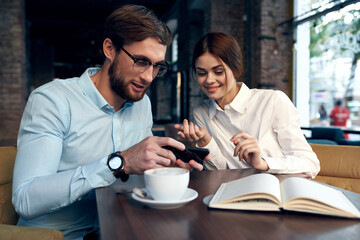 Cheerful man and woman are sitting in a cafe at the table working communication technology