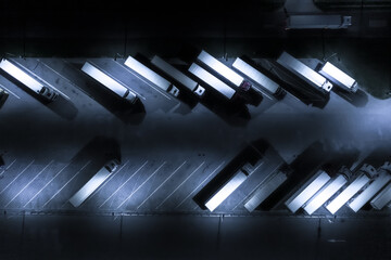 Aerial view of goods warehouse at Night. Logistics center in industrial city zone from above. Aerial view of trucks loading at logistic center. View from drone.