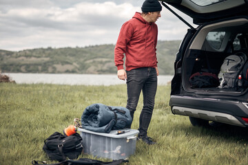 Camper packing and unpacking from a car's roof rack in nature.