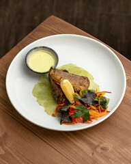 Plate of delicious food on wooden table. Fried white sea or river fish with greens and vegetables. Nice serving dish in restaurant. Top view. Vertical format.