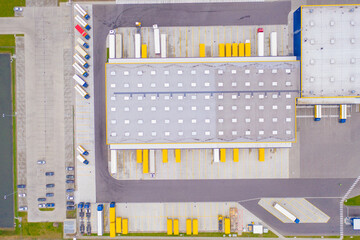 Aerial view of goods warehouse. Logistics center in industrial city zone from above. Aerial view of trucks loading at logistic center. View from drone.