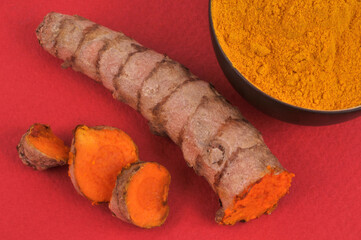 Curcuma frais coupé et bol de curcuma en poudre en gros plan sur fond rouge