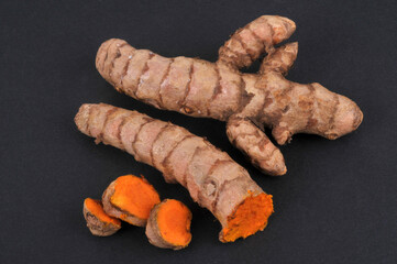 Curcuma frais entier et coupé en gros plan sur fond noir
